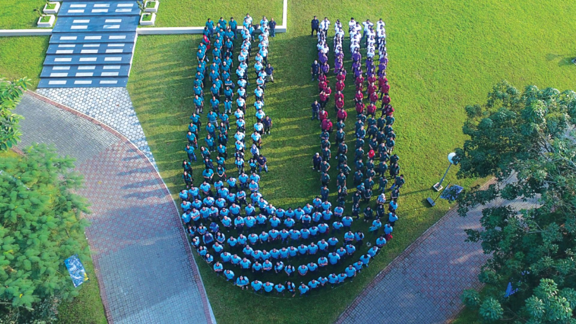 Aerial view of a group of people forming a large "U" shape on grassy ground.