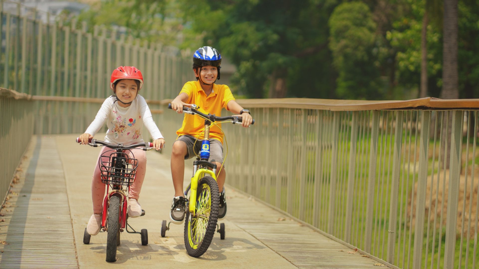 Two children, wearing helmets, smile as they ride bicycle together
