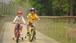 Two children, wearing helmets, smile as they ride bicycle together